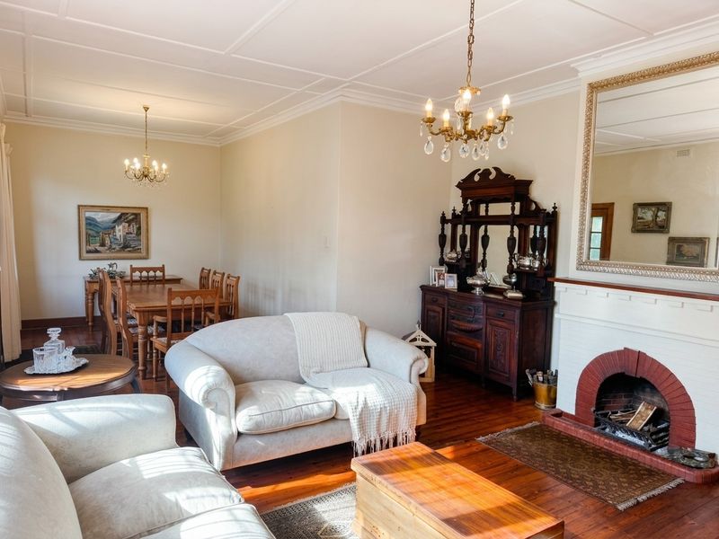 Spacious open-plan living and dining area featuring polished hardwood floors, a classic brick fireplace, and elegant ceiling detailing.