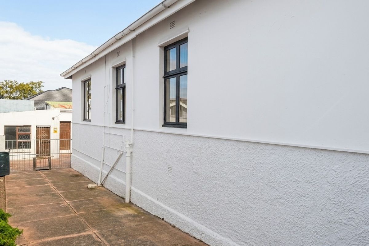 A view of the rear exterior of the property featuring a paved walkway, white textured walls, and a secure metal gate.