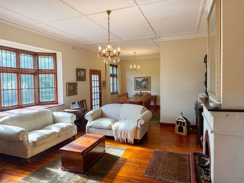 Spacious open-plan living and dining area featuring polished timber floors, a classic fireplace, leaded glass windows, and elegant coffered ceilings.