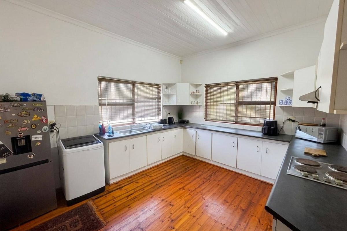 A functional kitchen featuring timber flooring, white built-in cabinetry, laminate countertops, a double sink, and a built-in hob with an extractor fan.