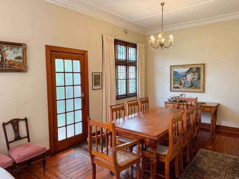 A traditional dining room featuring warm timber flooring, leaded glass windows, and a classic timber-framed glass door leading to the exterior.