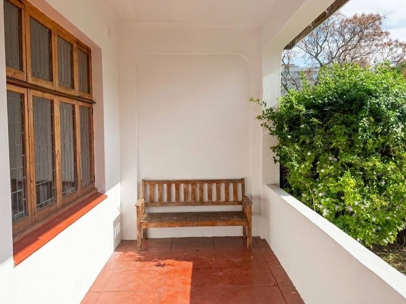 A covered patio area featuring terracotta floor tiles and timber-framed windows with leaded glass detailing, overlooking a garden.