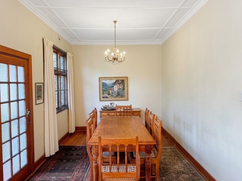 A formal dining room featuring original timber flooring, decorative ceiling detail, and a classic leaded glass window.