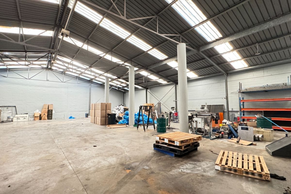 Spacious industrial warehouse featuring high ceilings with skylights, concrete flooring, and structural support columns, suitable for storage or manufacturing operations.