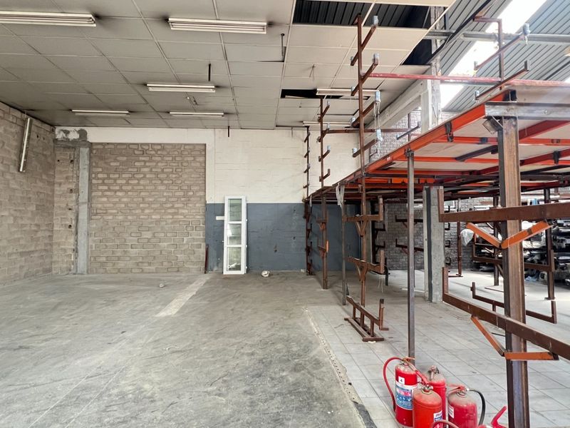 Spacious industrial utility area featuring exposed brick walls, concrete flooring, and integrated steel racking systems, suitable for storage or workshop operations.