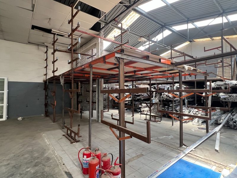 Industrial utility space featuring a mezzanine level, steel racking, exposed roof trusses, and skylights, suitable for storage or workshop operations.