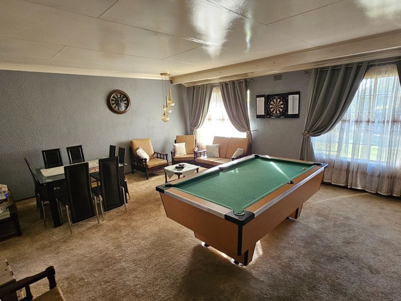 Spacious living area featuring carpet flooring and large windows, currently utilized as a multi-purpose entertainment and dining space.