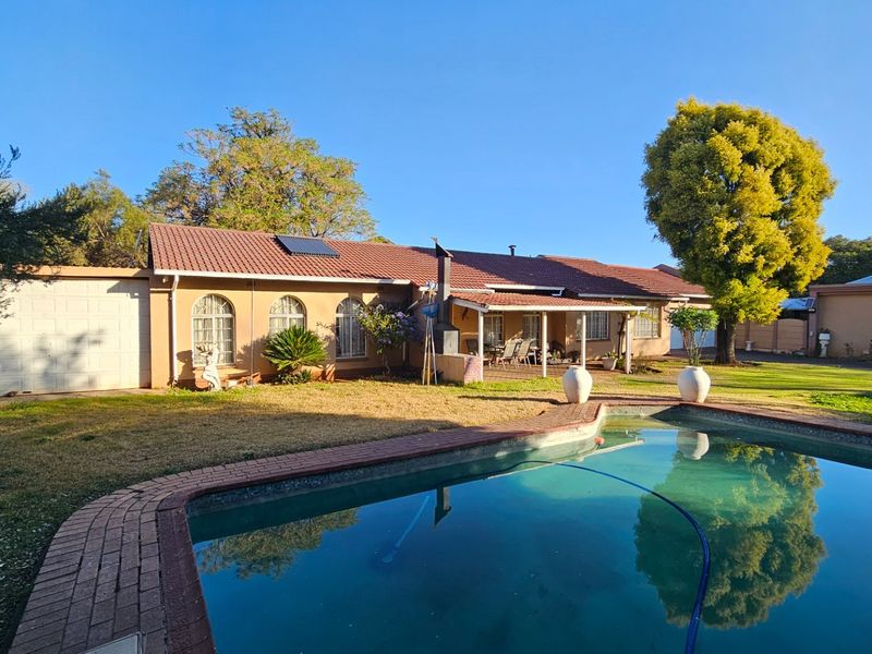 Rear view of the house featuring a swimming pool with brick coping, a covered patio area, and a tiled roof with solar heating panels.