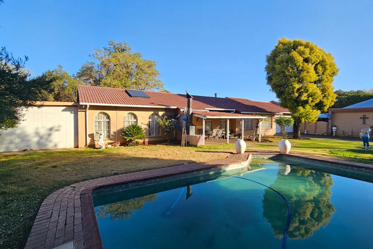 Rear view of the house featuring a swimming pool with brick coping, a covered patio area, and a tiled roof with solar heating panels.