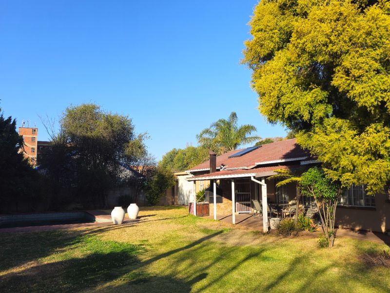 Rear view of the property featuring a covered patio, a swimming pool, and a spacious garden area with mature trees.