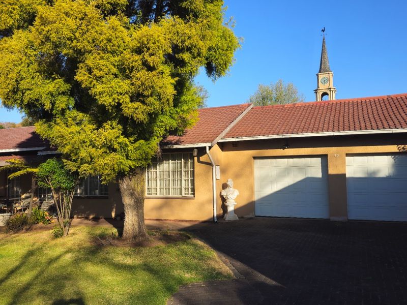 Front view of the property featuring a double garage, paved driveway, and a well-maintained garden area with mature trees.