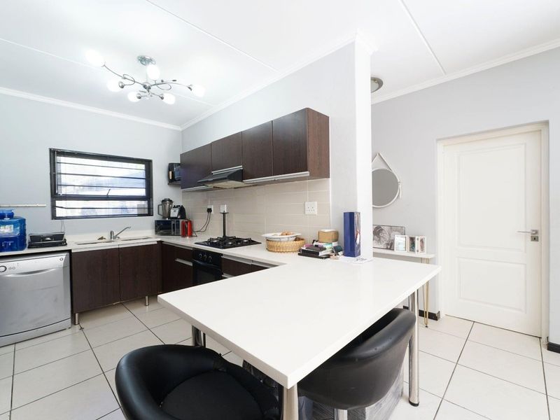 A functional kitchen featuring dark wood cabinetry, a gas hob with extractor, tiled flooring, and a convenient breakfast counter for casual dining.