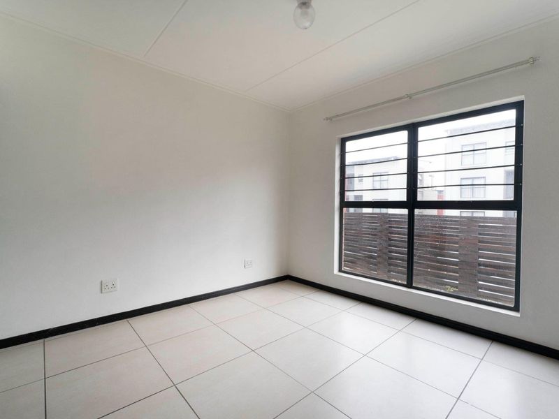 A clean, empty bedroom featuring neutral tiled flooring, white walls, and a window fitted with security bars.