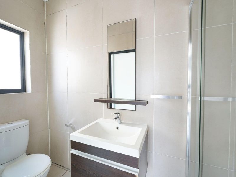A modern, clean bathroom featuring a vanity cabinet with a basin, a glass-enclosed shower, and neutral wall tiling.