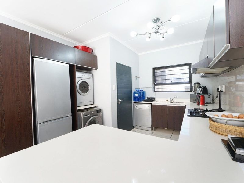Modern kitchen featuring dark wood cabinetry, stone countertops, integrated laundry space, gas hob, extractor fan, and tiled flooring.