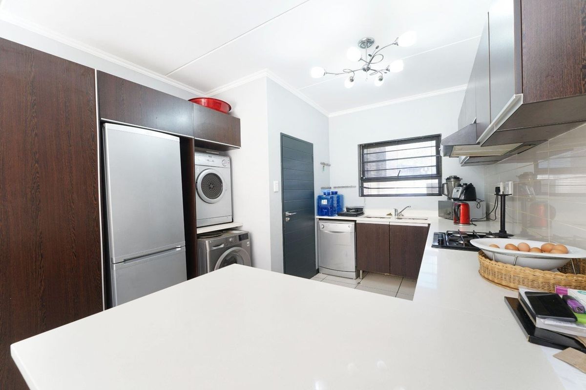 Modern kitchen featuring dark wood cabinetry, stone countertops, integrated laundry space, gas hob, extractor fan, and tiled flooring.