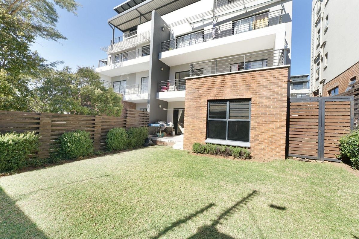 Rear view of a modern apartment building featuring a private garden, brick facade, and multiple balconies with metal railings.