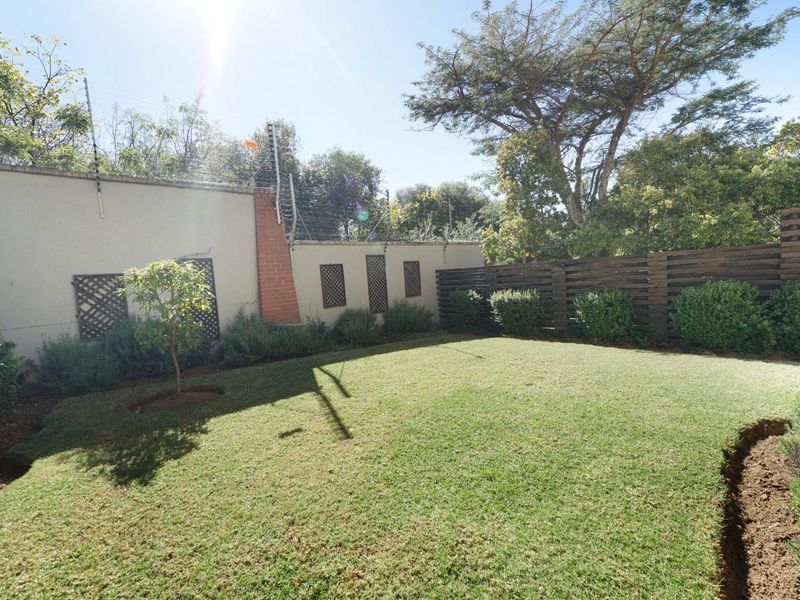 A well-maintained private garden featuring a manicured lawn, perimeter wall with electric fencing, and timber slat privacy screening.