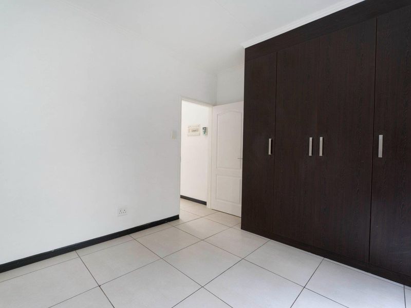 A clean, empty bedroom featuring neutral tiled flooring and dark wood built-in cupboards, offering a blank canvas for personalization.