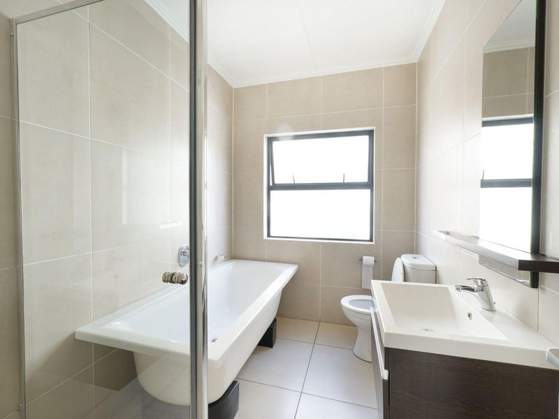 A clean, modern bathroom featuring a freestanding bathtub, glass-enclosed shower, vanity with basin, and neutral floor-to-ceiling tiling.