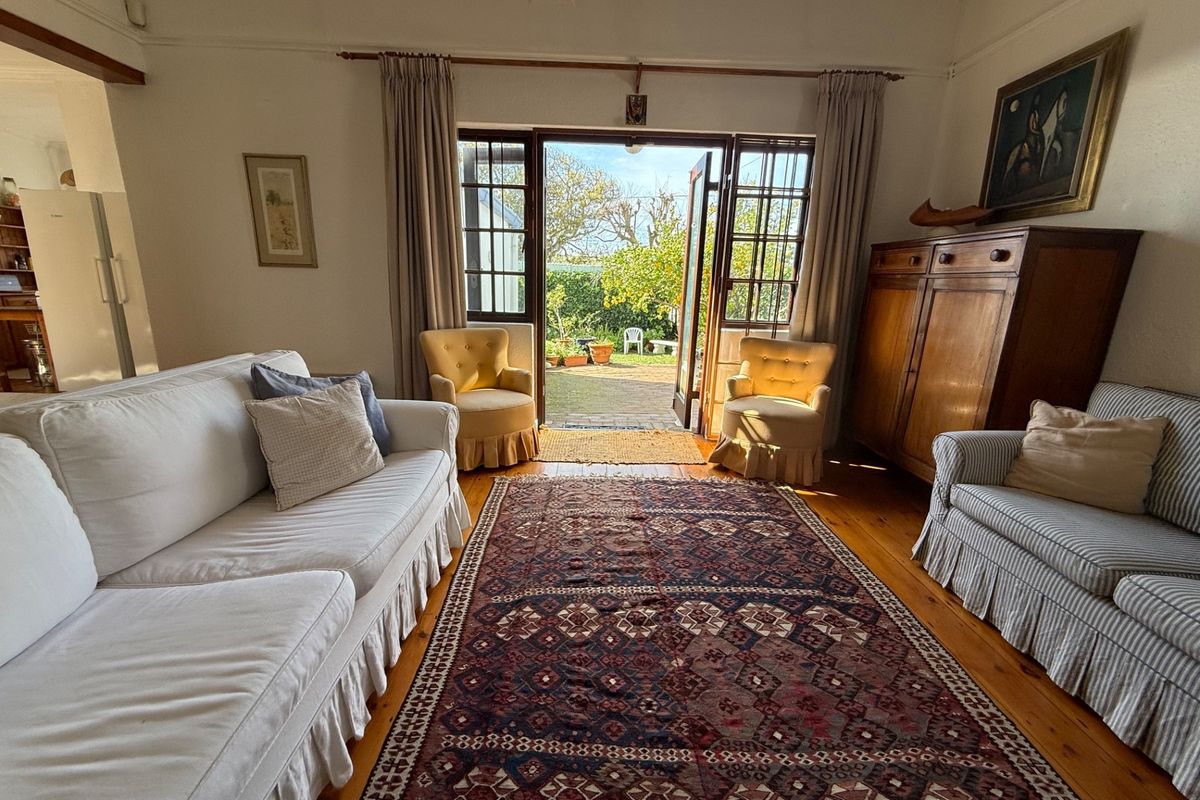 A bright living room featuring original hardwood flooring and classic french doors that open directly onto a rear patio and garden area.