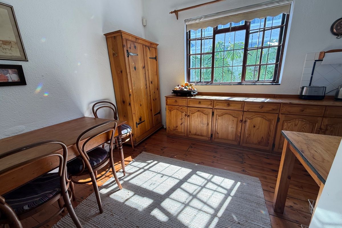 A rustic kitchen area featuring traditional wooden cabinetry, timber flooring, and a large window with security bars, offering a warm and classic aesthetic.