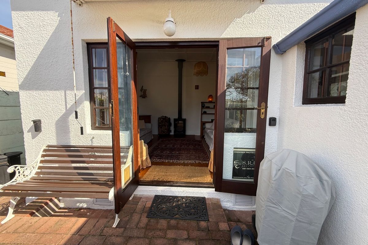 Rear exterior view showing brick paved patio area leading through timber french doors into a living space with a wood burning stove.