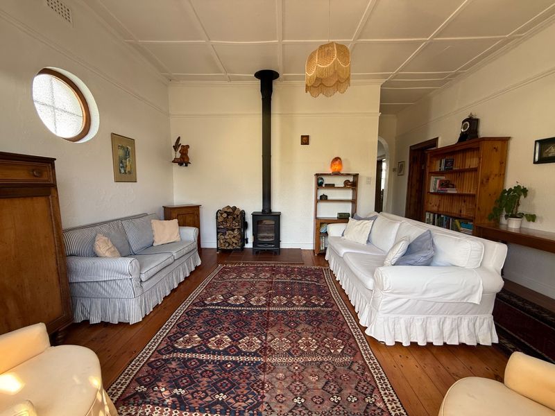 A cozy living room featuring a wood-burning stove, original timber flooring, and a distinctive coffered ceiling with a circular window.