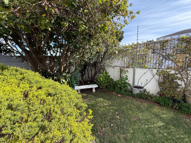 A private garden area featuring a well-maintained lawn, mature trees, and secure perimeter walling with electric fencing.