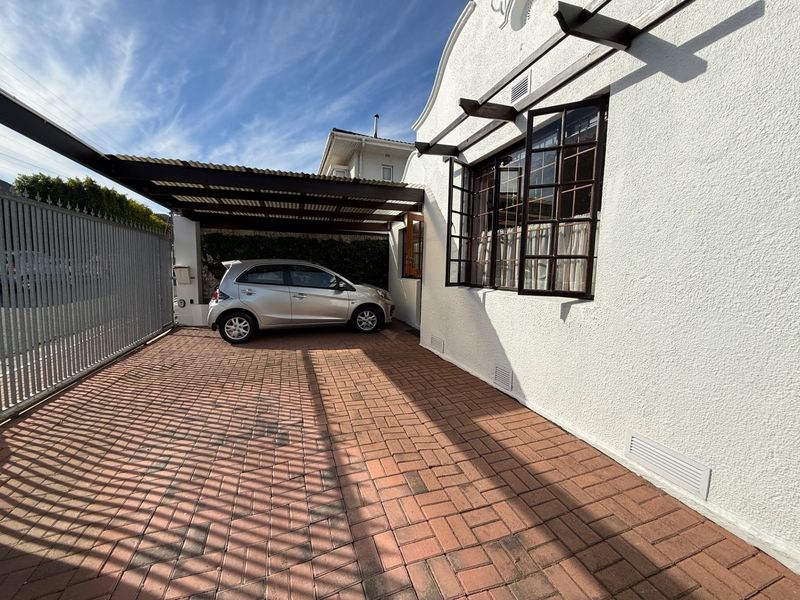A well-maintained front exterior featuring a paved driveway, a covered carport, and a classic white stucco facade with timber-framed windows.