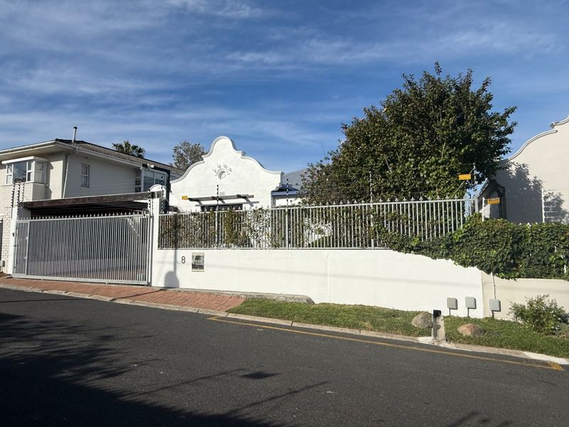 Front elevation of a house featuring a gabled facade, secure metal perimeter fencing with electric wires, and a private driveway gate.