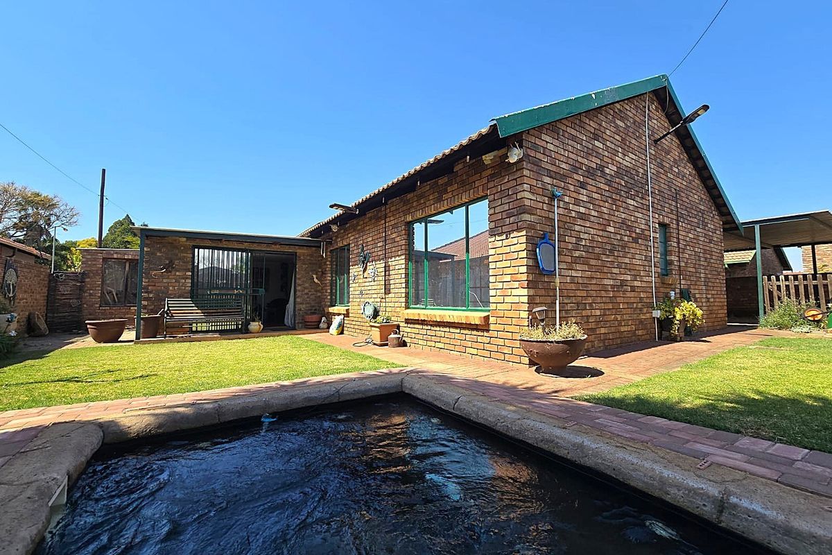 Rear view of a face brick house featuring a swimming pool, paved pathways, and a small garden area.