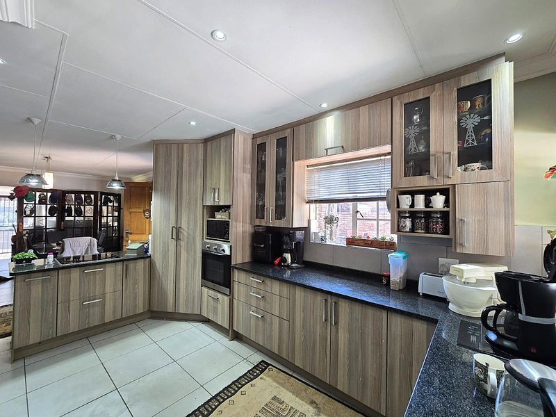 A well-maintained kitchen featuring modern wood-grain cabinetry, granite countertops, built-in oven and microwave, and recessed lighting, seamlessly flowing into the adjacent living area.