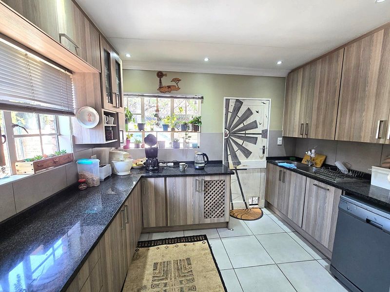 A functional kitchen featuring wood-look laminate cabinetry, dark granite countertops, tiled flooring, and ample natural light from multiple windows.