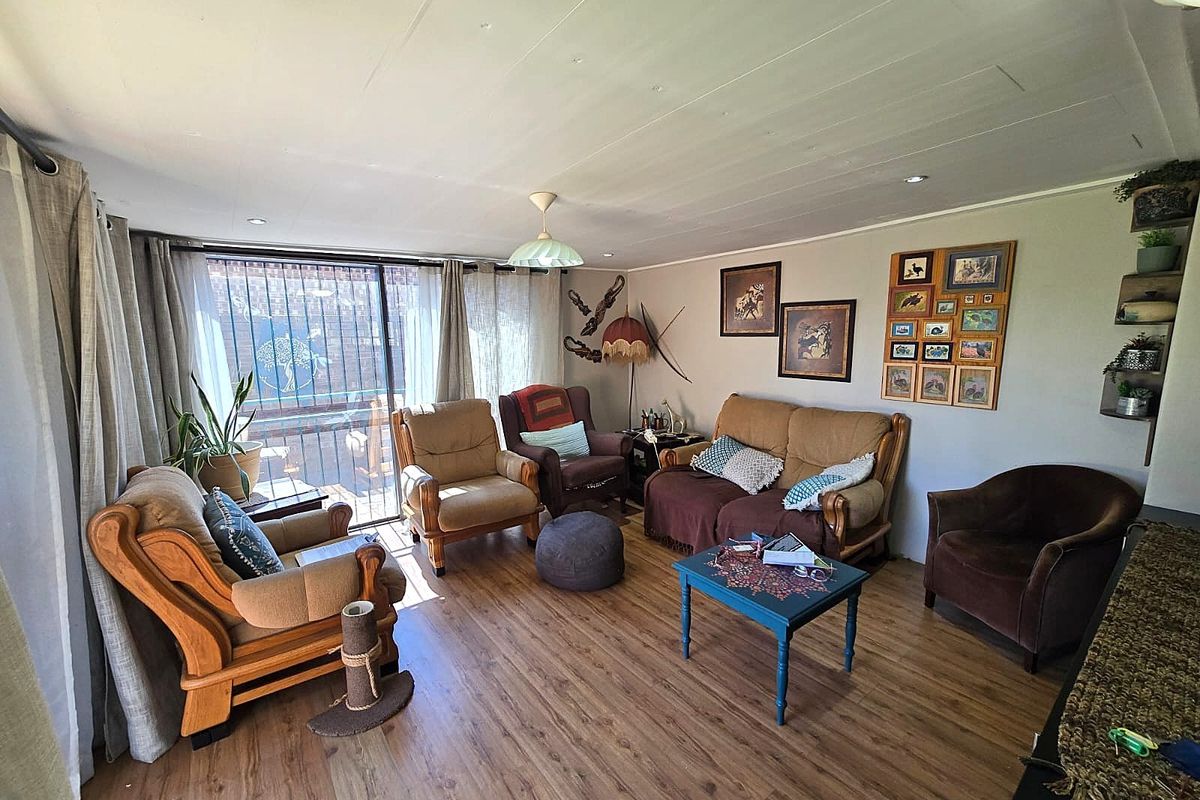 A comfortable living room featuring laminate flooring, recessed lighting, and a large sliding glass door with security gate providing access to the exterior.