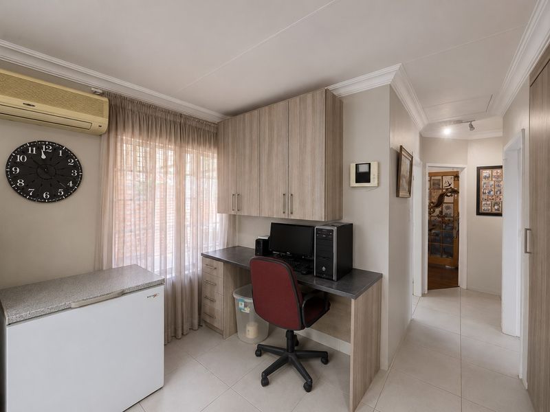 A functional home office space featuring built-in desk and cabinetry, tiled flooring, and a wall-mounted air conditioning unit.