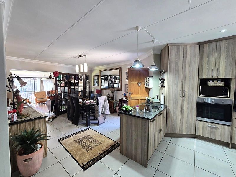 Open-plan kitchen and dining area featuring modern wood-finish cabinetry, granite countertops, built-in appliances, and tiled flooring throughout.