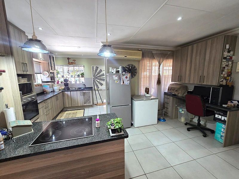 Open-plan kitchen featuring wood-look cabinetry, granite countertops, an electric hob, and integrated workspace, finished with neutral floor tiles and recessed lighting.