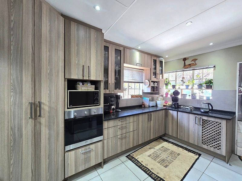 A functional kitchen featuring wood-look laminate cabinetry, granite countertops, built-in oven, and microwave, complemented by tiled flooring and recessed lighting.
