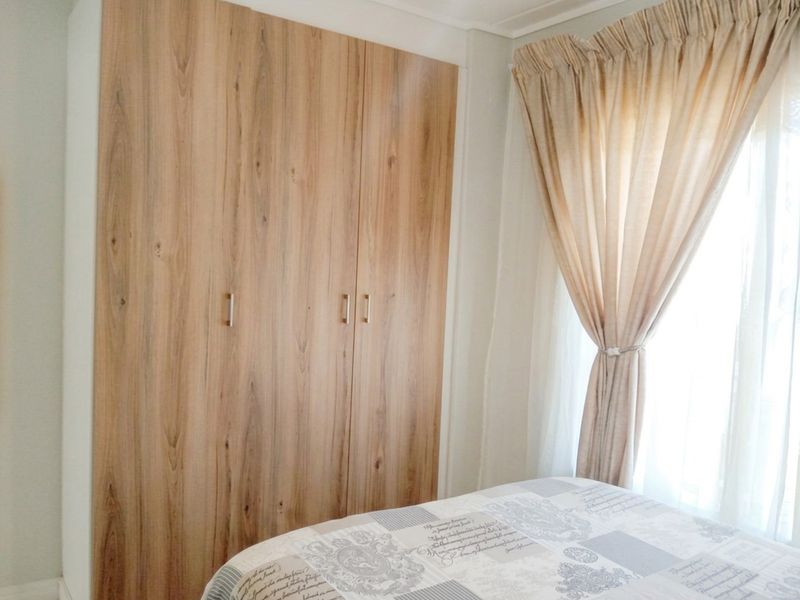 A bedroom featuring a modern wood-finish built-in wardrobe and natural light from the adjacent window.
