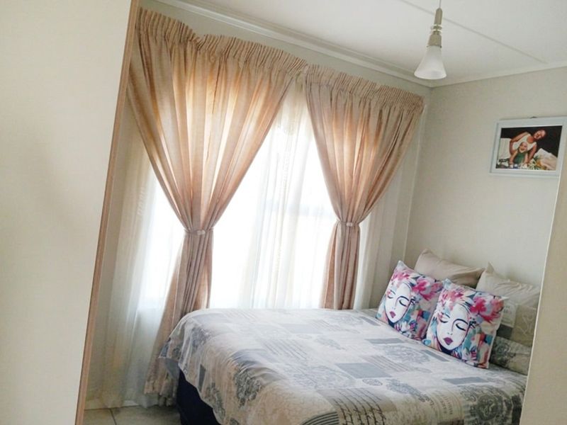 A cozy bedroom featuring tiled flooring, a central pendant light, and large window with curtains, providing a comfortable and functional sleeping space.