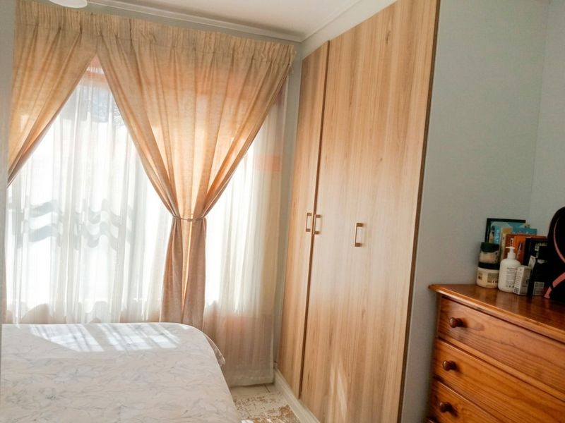 A bedroom featuring a light wood-finish built-in wardrobe and a window with curtains, providing natural light to the space.