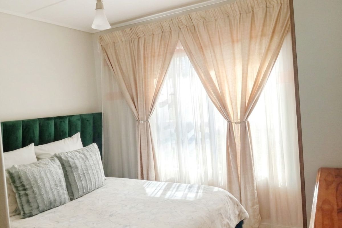 A bright and well-maintained bedroom featuring large windows with layered curtains and a central pendant light fixture.