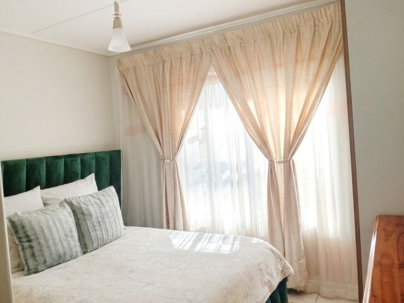 A bright and well-maintained bedroom featuring large windows with layered curtains and a central pendant light fixture.