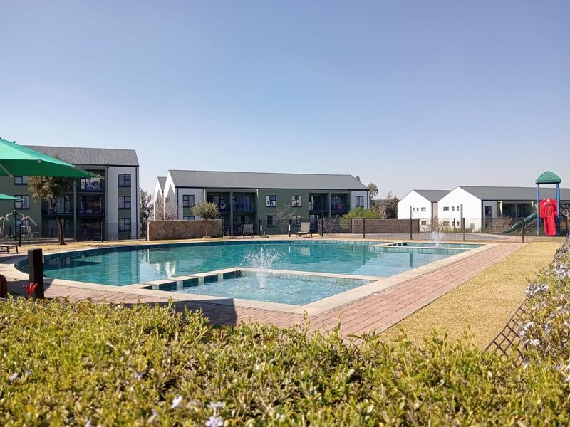A well-maintained communal swimming pool area featuring a water fountain, paved surround, and landscaped garden, set within a modern apartment complex.
