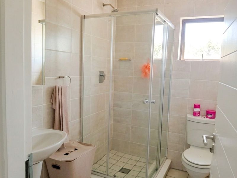 A functional bathroom featuring a glass-enclosed shower, pedestal basin, and toilet with neutral wall and floor tiling.
