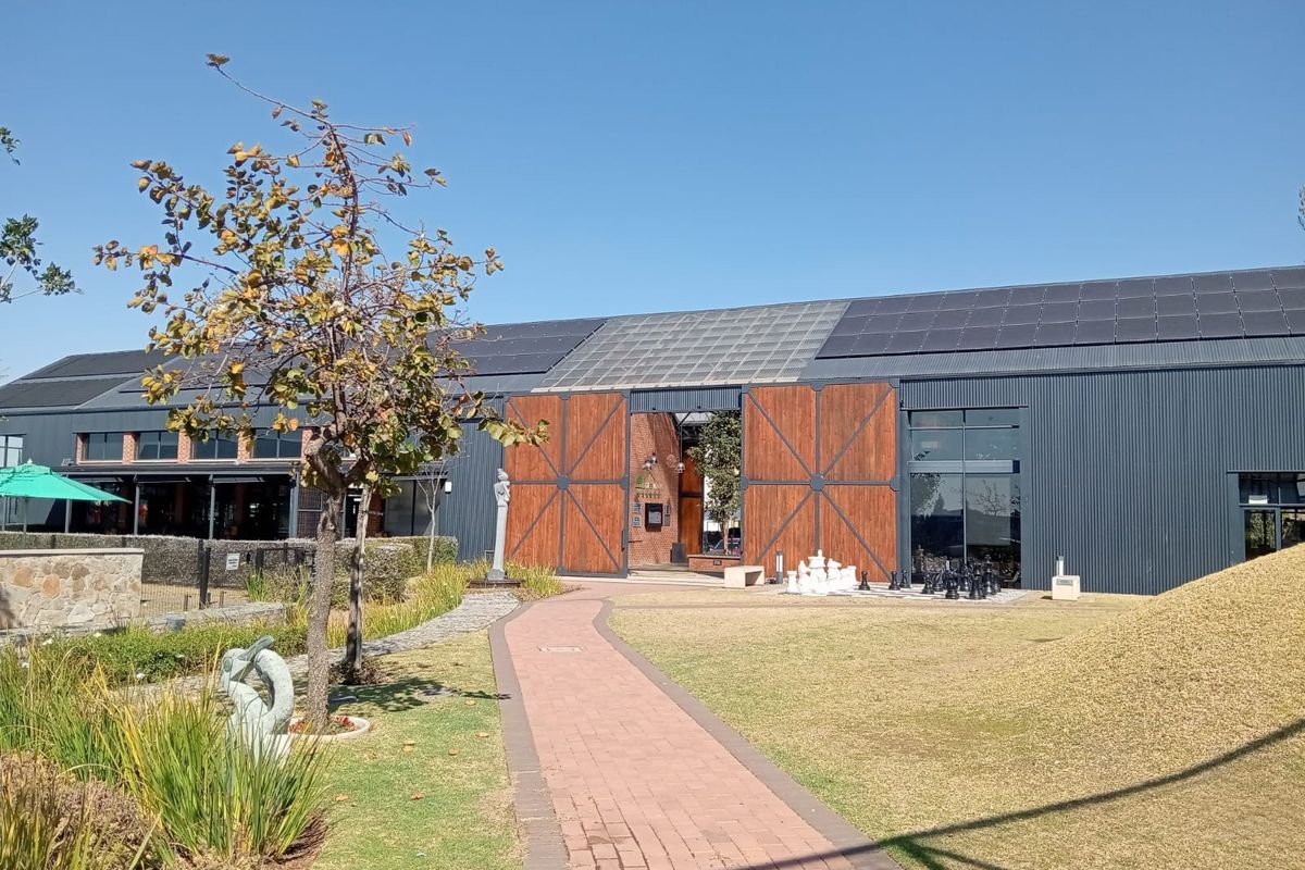 A well-maintained exterior view of a modern industrial-style building featuring corrugated metal cladding, solar panels, and large wooden barn doors opening to a landscaped garden.