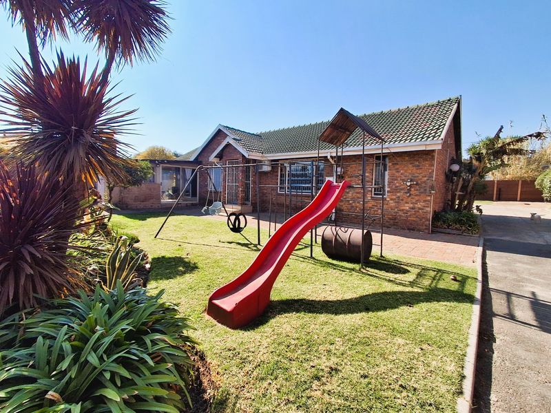 Rear view of the brick house featuring a tiled roof, paved patio area, and a well-maintained garden space.