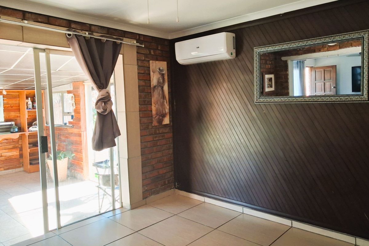 A bright living area featuring tiled floors, an exposed brick wall, timber paneling, and a split-system air conditioner, with access to an outdoor patio.