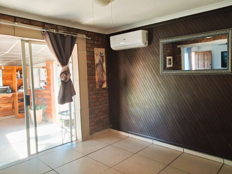 A bright living area featuring tiled floors, an exposed brick wall, timber paneling, and a split-system air conditioner, with access to an outdoor patio.